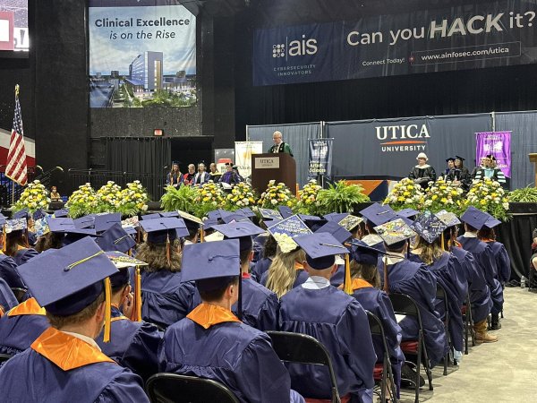 Members of the Class of 2024, in caps and gowns, sit in the Utica Memorial Auditorium as President Todd Pfannestiel speaks from a podium.