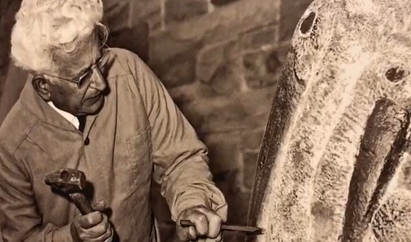 Black and white image of Henry Dispirito at work on a sculpture, with hammer and chisel in hand.