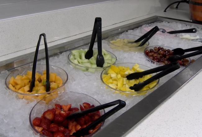 Bowls of various types of sliced fruit sitting in a cooler of ice, with tongs.