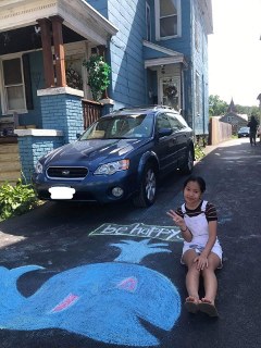 A Young Scholar poses with a picture of the whale she drew in her home's driveway.