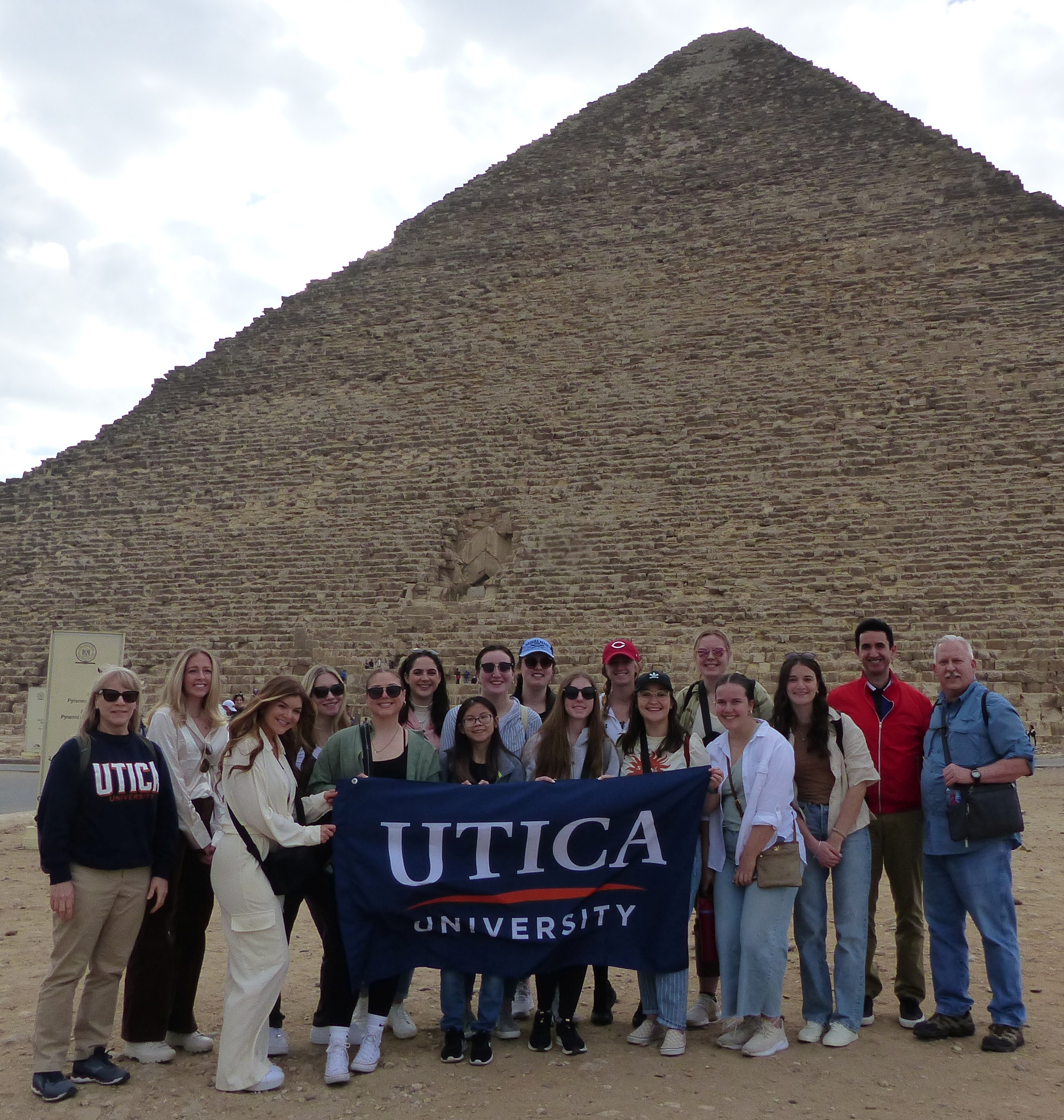 Students and Faculty hold up a Utica University banner at the Great Pyramid during a January 2023 visit to Egypt.