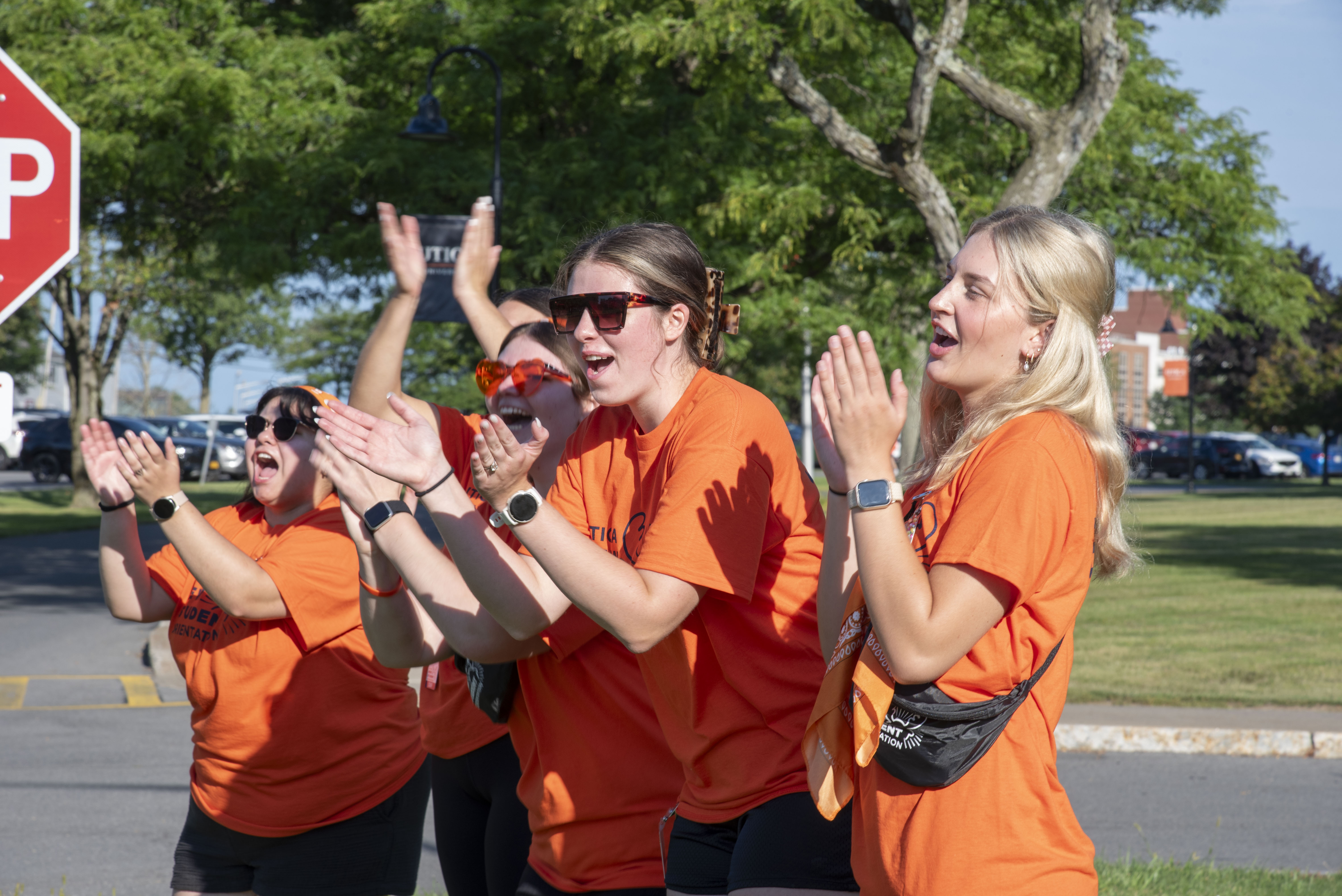 Students in orange t-shirts clap and shout happily for newcomers to campus.
