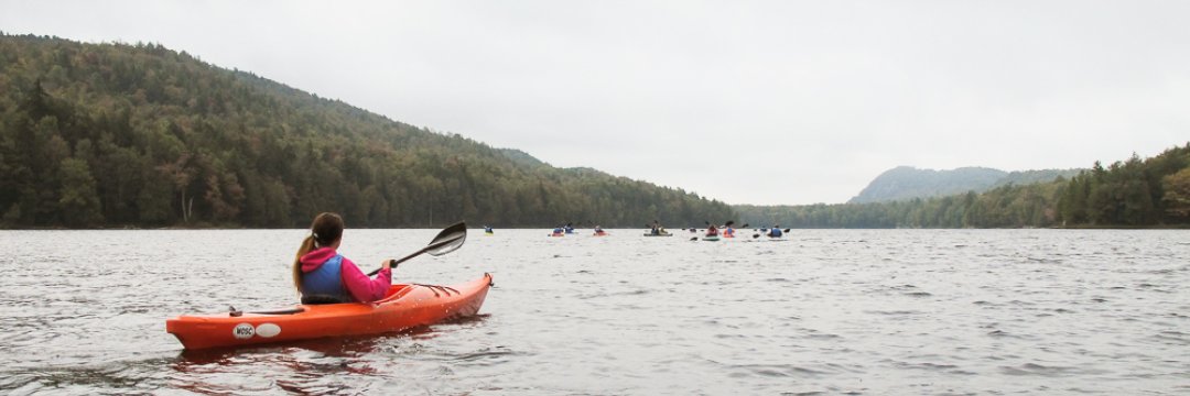 A young woman in a hooded sweatshirt and vest kayaking on the water.
