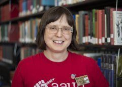 Katie Spires in glasses and red shirt stands in front of library stacks.