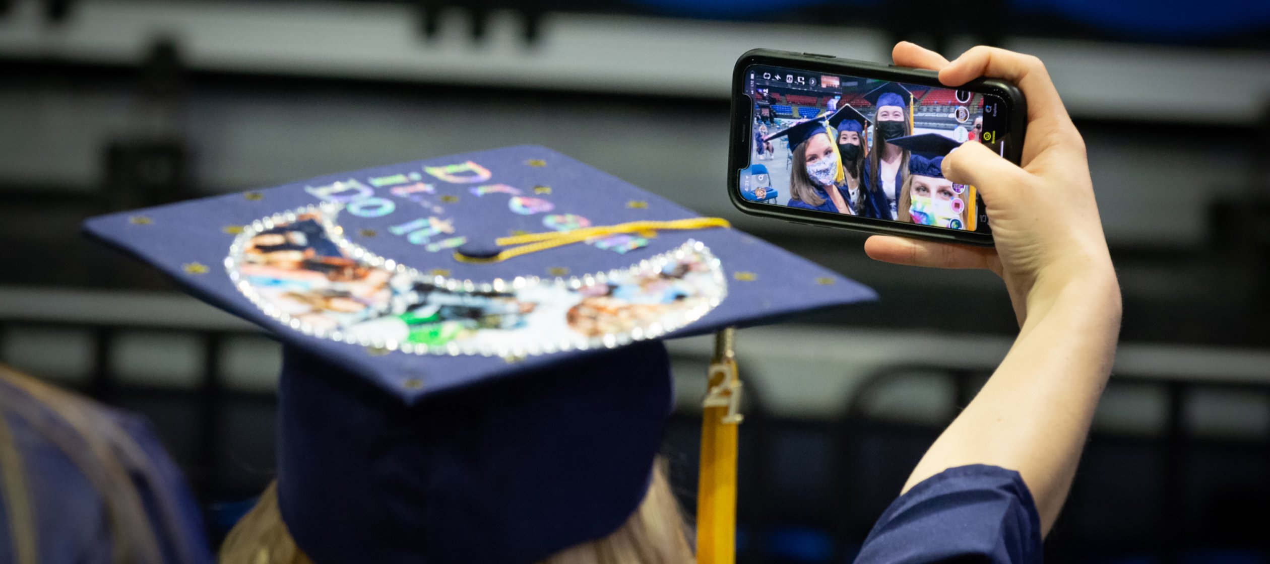 Student at the 2021 Commencement Ceremony takes a photo with a smartphone with classmates.