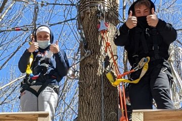 Students give thumbs up while on platform of outdoor ropes course.