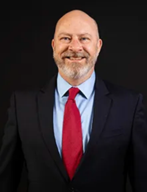 Paul Doeg in red tie, blue shirt and suit, smiles at camera.