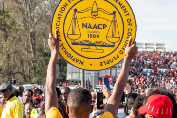 Person holding a yellow NAACP logo sign at a rally.