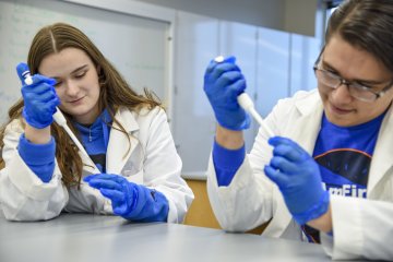 Students Nathan Rice ’24 and Lexi Lumley ’24 conduct research in labcoats and blue gloves.