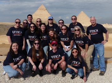 Students and Faculty wearing Utica t-shirts stand in front of the pyramids during a January 2023 trip to Egypt.