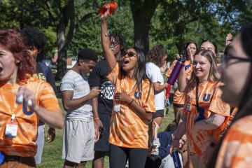 Students in orange t-shirts smile and cheer at the start of Convocation 2026.