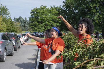Cars lined up to unload at Residence Halls as current students cheer for them by the sidewalk.
