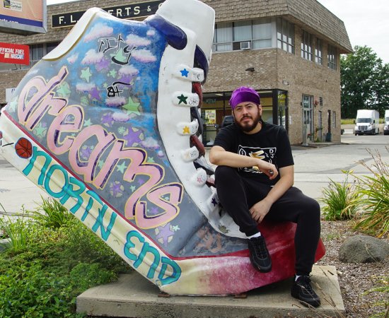Samson Maldonado poses next to giant shoe with word "dreams" on it.