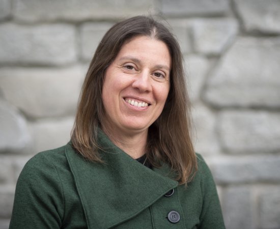 Sara Scanga, smiling, standing in front of a stone wall.