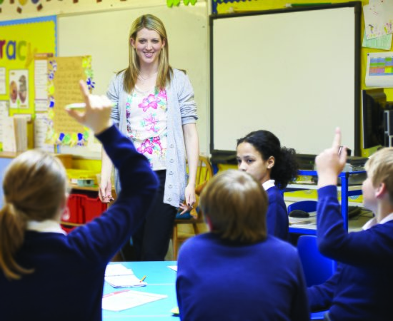 Teacher in a classroom with students raising their hands.