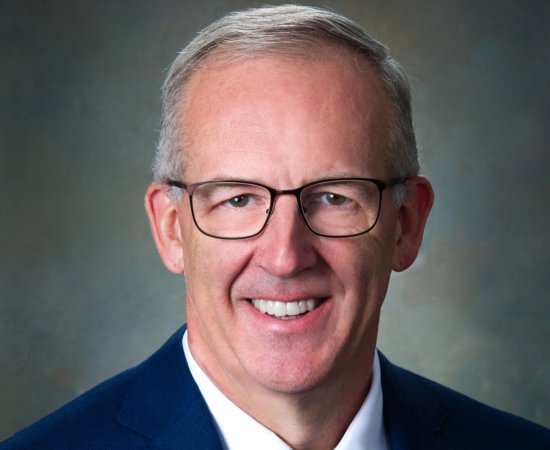 Greg Sankey, a man with short cut gray hair in glasses and blue suit, smiles at camera.