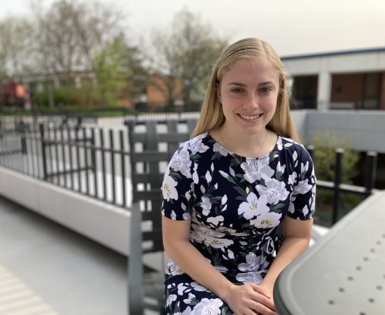 Isabelle LaBelle '23, in floral dress, sits at a table in the courtyard outside the library.