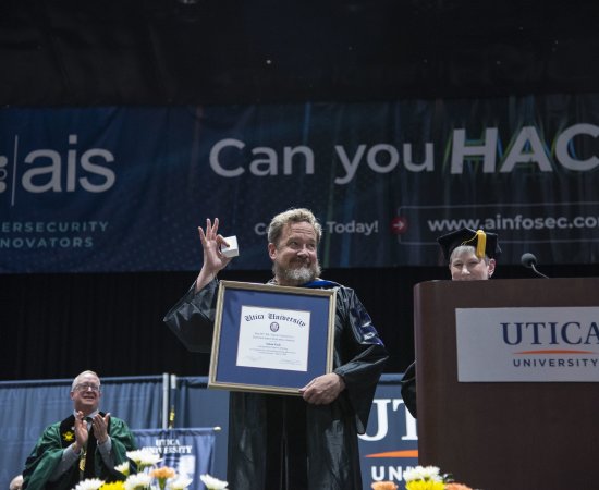 Dr. Adam Pack holds up the framed Crisafulli Award at the 2024 Commencement Ceremony.
