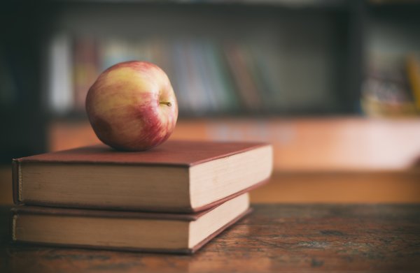 Apple sitting on a pile of books on a classroom desk.