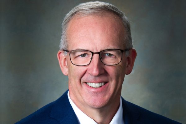 Greg Sankey, a man with short cut gray hair in glasses and blue suit, smiles at camera.