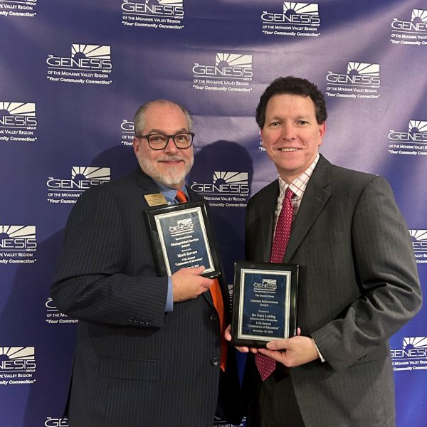 Mark Kovacs and Gary Leising hold up plaques at the Genesis Group's Celebration of Education event in November 2023.