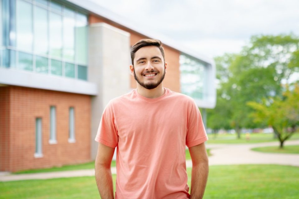 Communication and Media major and Editor-in_chief of The Tangerine, Matthew Breault, stands on campus, smiling at camera.