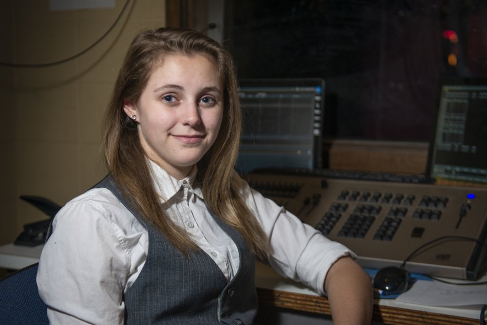 Crystal Hayner, with long brown hair, wearing a vest, sits by a computer set-up.