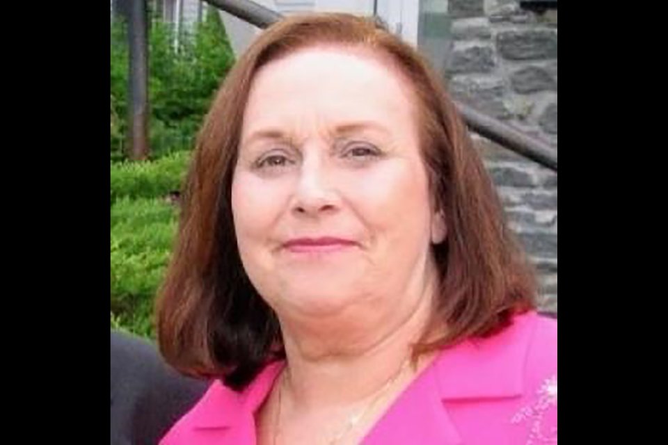 Lyn Simon, a woman with shoulder-length auburn hair, wearing a pink lapeled jacket, smiles at the camera.