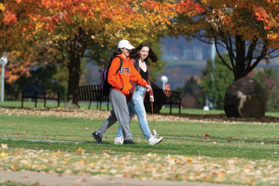 Two students walk across campus amid the red, orange and yellow trees of Autumn.