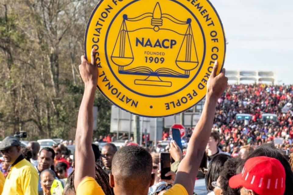 Person holding a yellow NAACP logo sign at a rally.