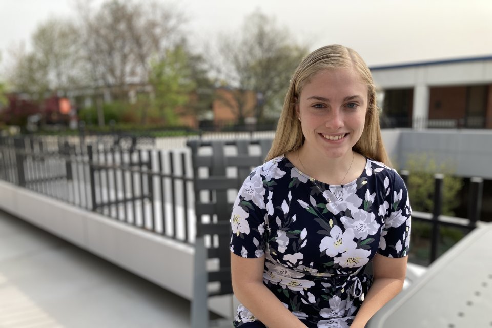 Isabelle LaBelle '23, in floral dress, sits at a table in the courtyard outside the library.