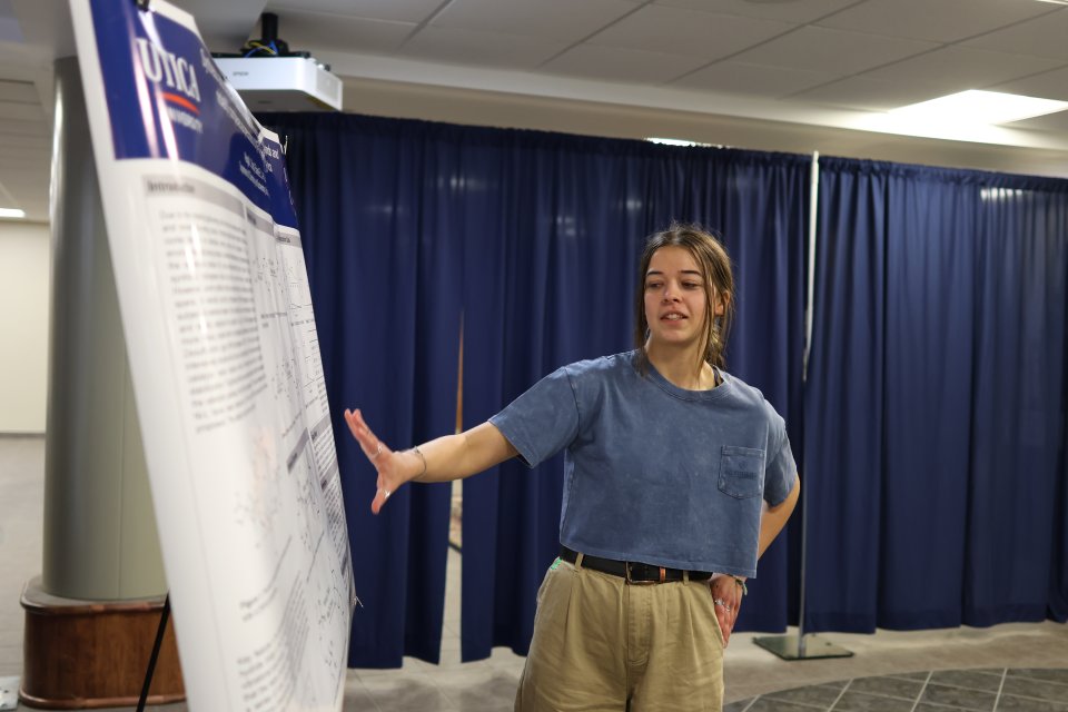 A student makes a presentation beside a poster at the 2024 Student Conference for Research, Professional Activities, and Creative Arts