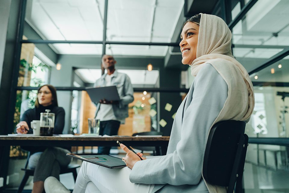 Woman smiling in a business meeting around a table with other professionals.