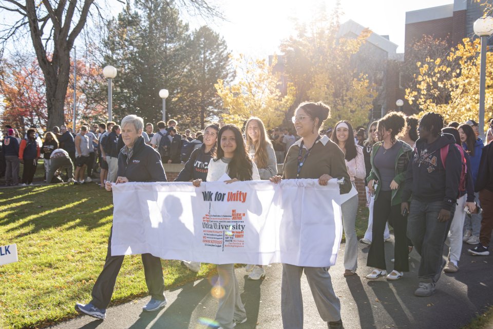 President Nesbitt, student Madison Jordan, and Director of Community, Belonging and Engagement Kira Maddox carry a banner as a crowd of students, faculty, and staff follow behind them.